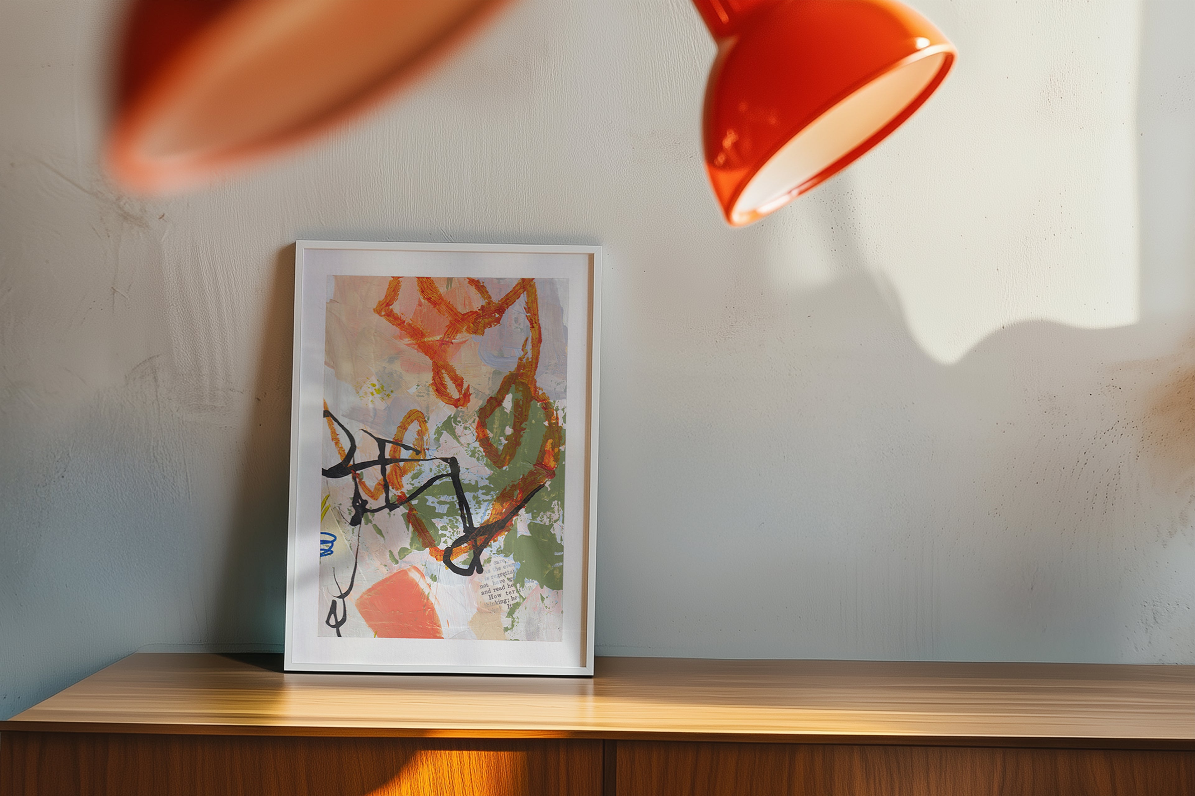 Framed abstract art on a wooden shelf with a red lampshade casting a shadow on the wall.